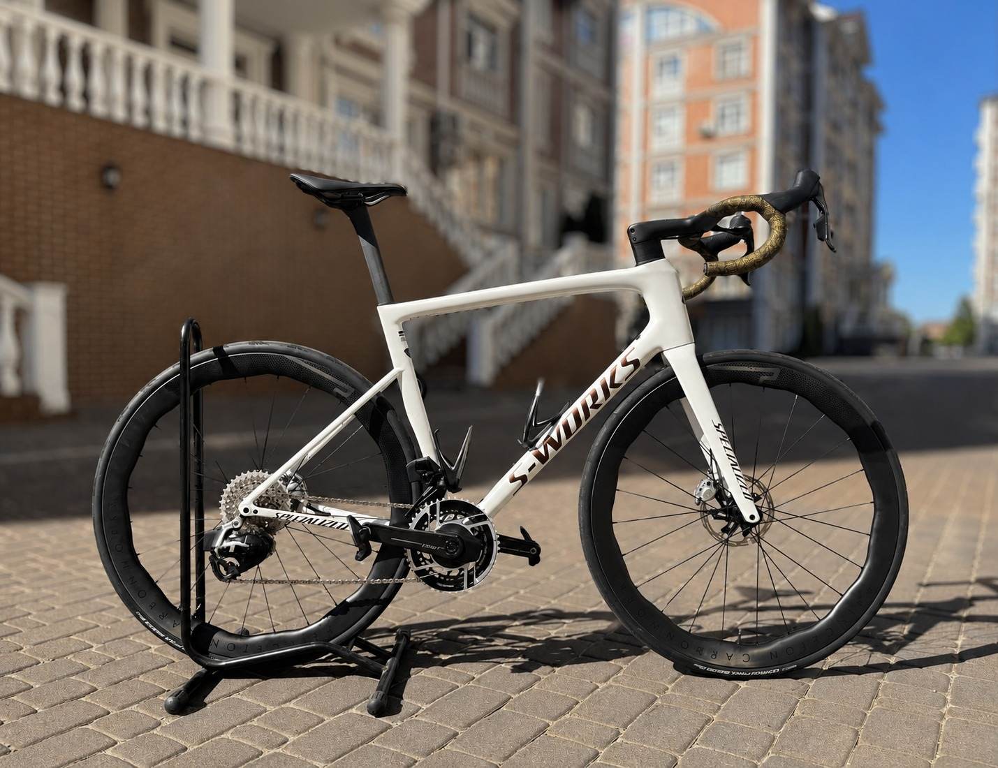 Білий шосейний велосипед S-Works Tarmac SL8 на підставці надворі, сонячний день, мідно-золоті декалі S-WORKS на нижній трубі